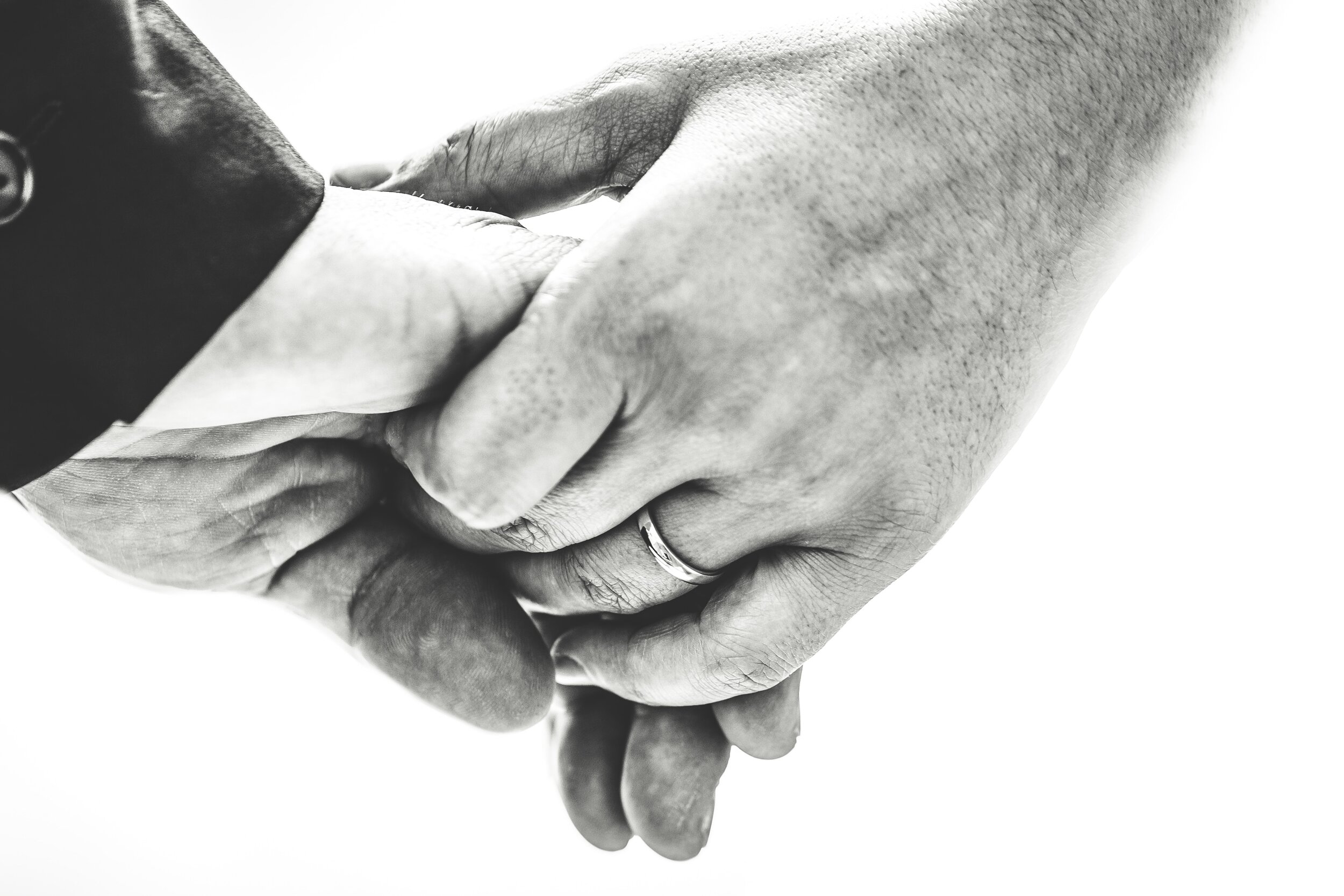 Black and white hands holding with wedding band against white background