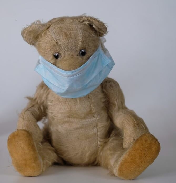 Vintage teddy bear with glass eyes wearing blue surgical mask