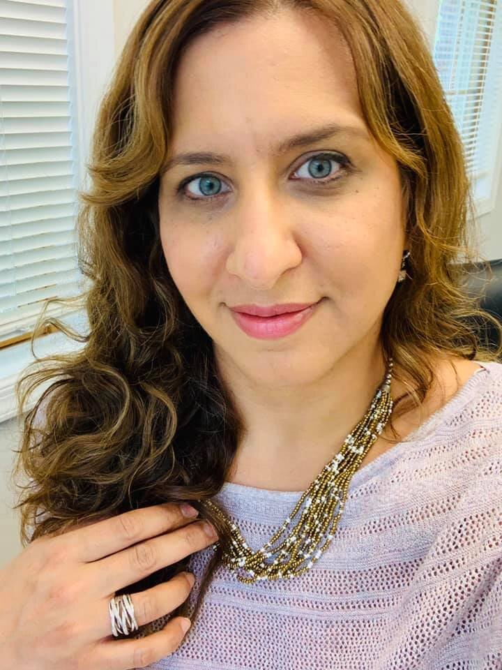 Woman with caramel highlights wearing lavender sweater and gold beaded necklace selfie